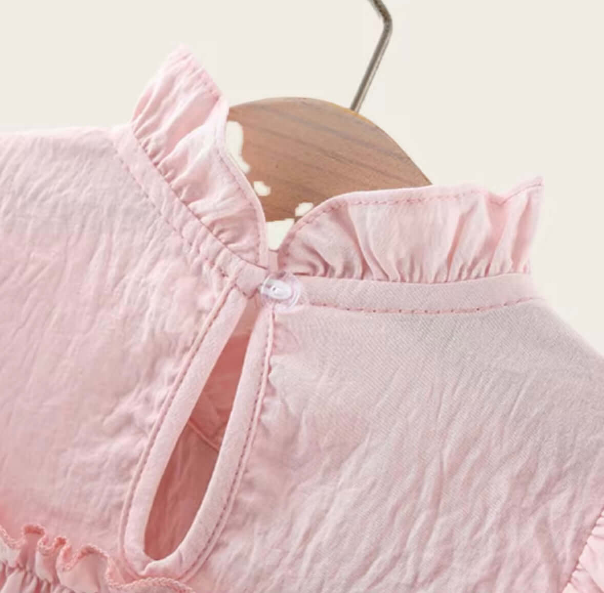 Close-up view of a blush pink ruffle dress displaying delicate flutter sleeves and a button closure.