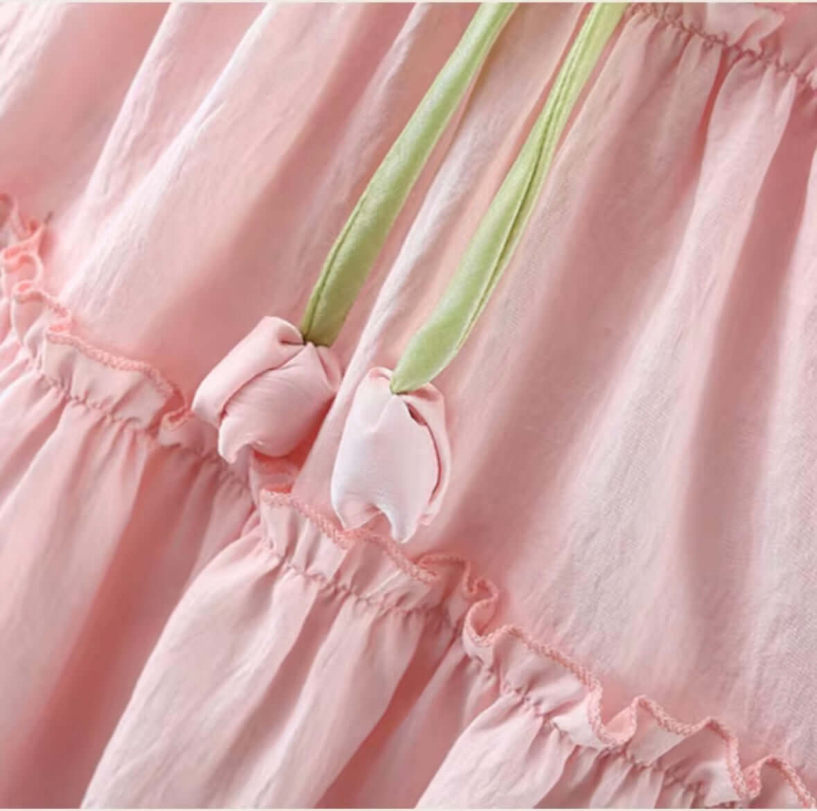 Blush pink ruffle dress featuring green bow tie and tulip accents, perfect for whimsical moments.