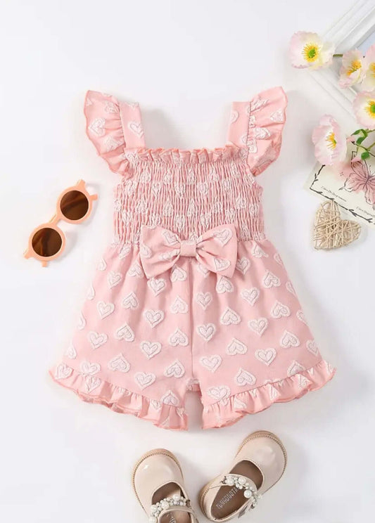 Pink heart-patterned girls' romper with bow detail, ruffled straps, perfect for playdates and sunny days.