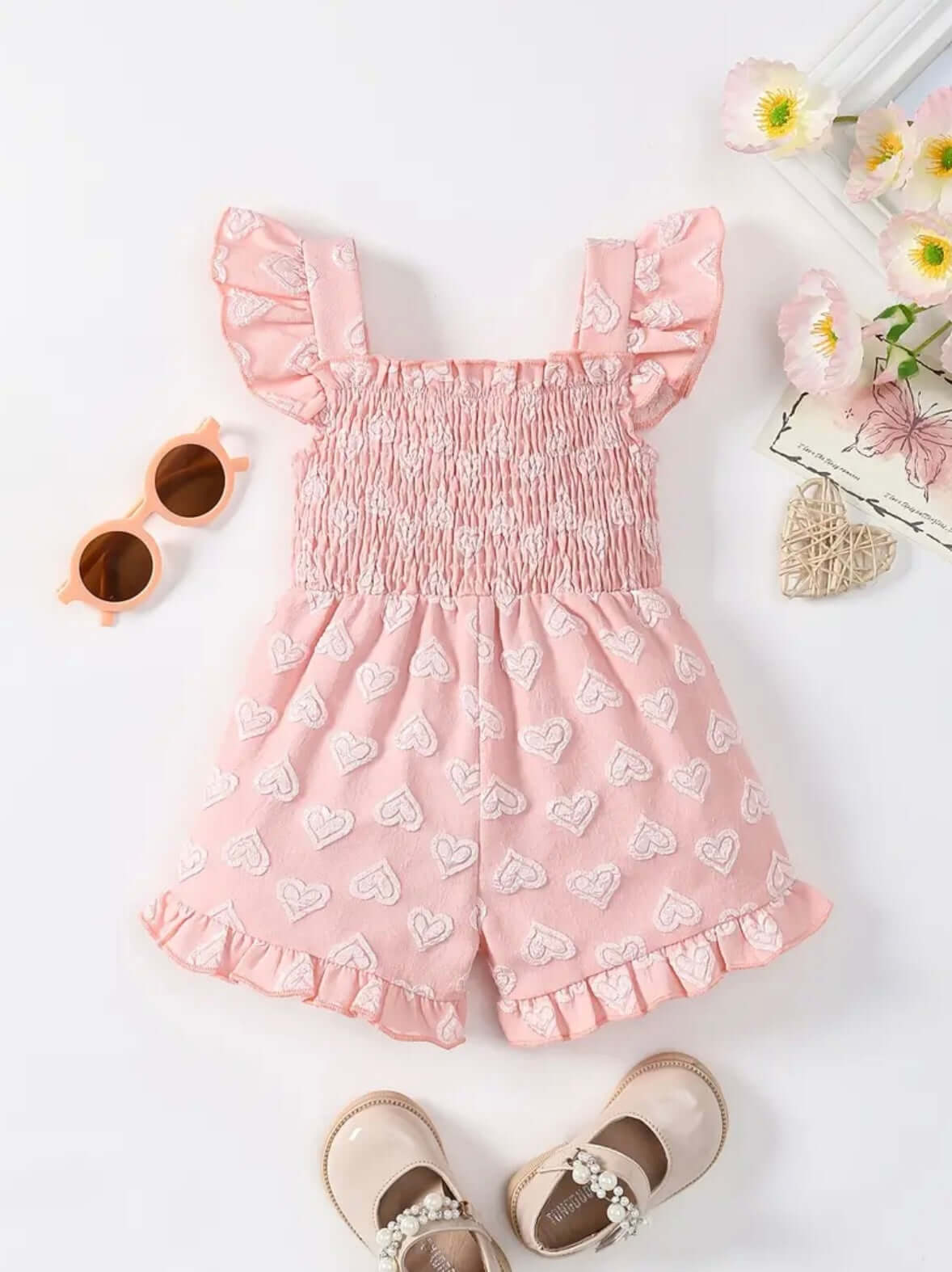 Adorable pink heart-patterned girls' romper with bow detail, perfect for summer playdates and outings.