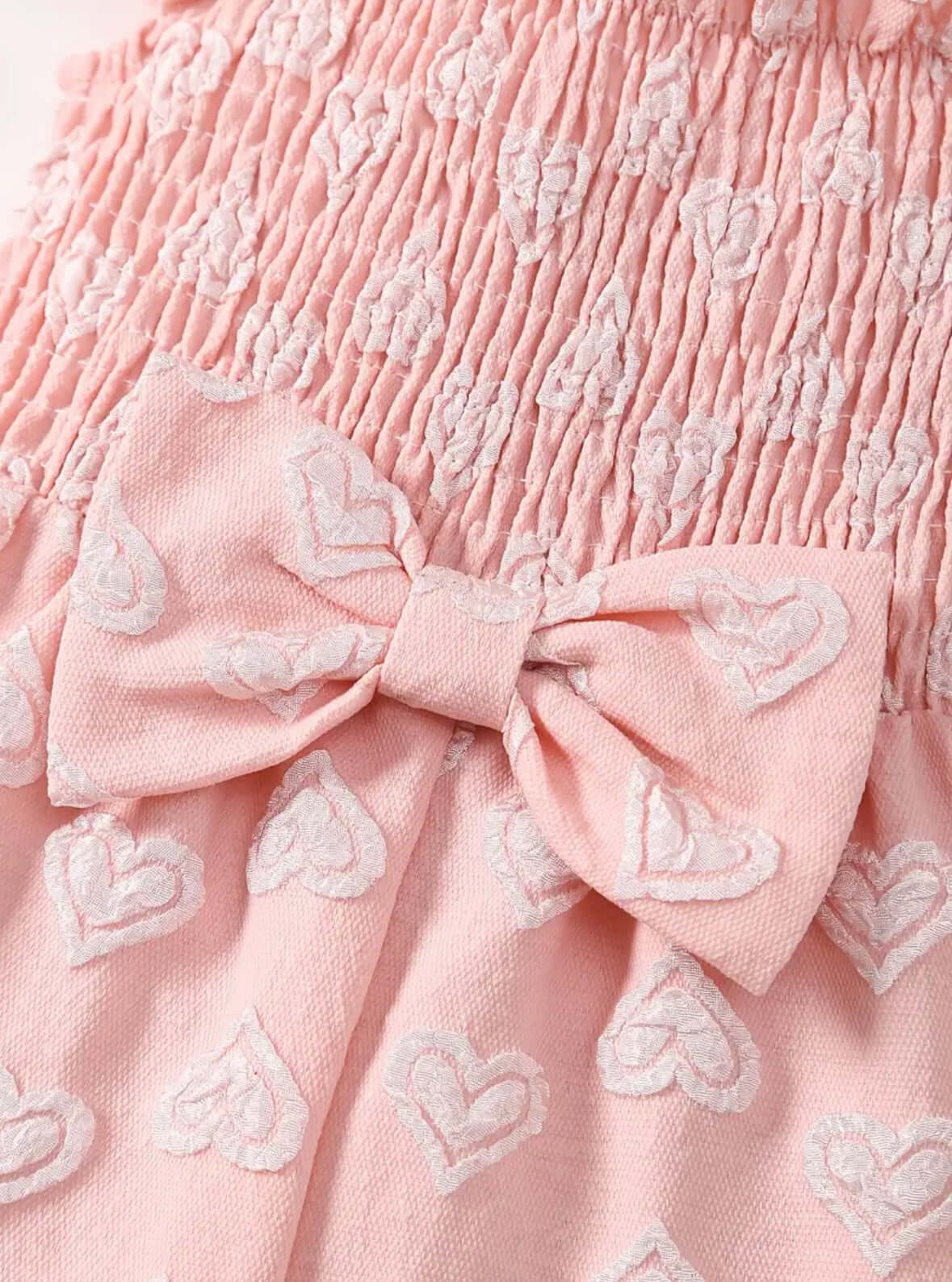 Close-up of pink heart-patterned fabric with a bow detail for girls' romper, showcasing soft material and playful design.